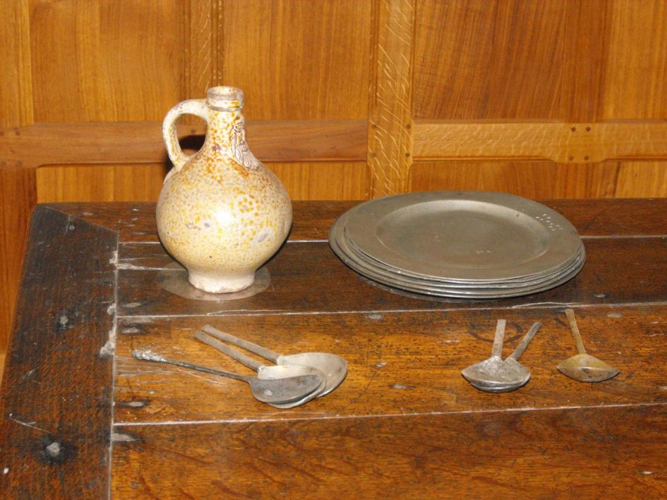 Pewter plates and spoons. The stoneware bellarmine flagon has a bearded face of a man on it.
