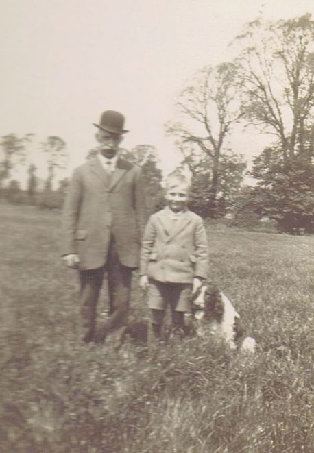 George Weedon and his grandson Bernard Lake.The picture is taken in the middle of the meadow behind 28 and 30 Shillington Road. The tall foreground trees on the right are elms, which died from Dutch Elm Disease in the 1970s. The moderately tall trees beyond them are pear trees in the old Wright’s Farm orchard. The bushes just to the left of George’s right elbow are brambles on the corner of the orchard, where the meadow boundary makes a dog-leg and the culvert under the meadow comes out, wrongly marked as a spring on the Ordnance maps.